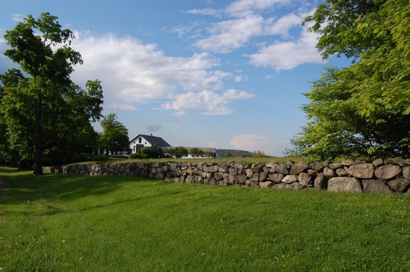 stone wall in front of white barn and blue sky overhead